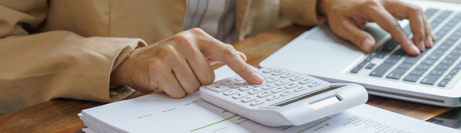 a person typing on a calculator and a laptop computer.