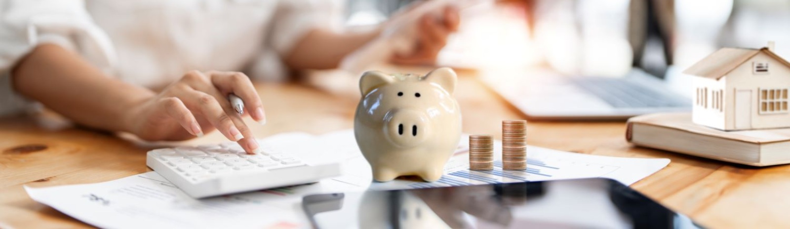 a person using a calculator, next to a piggy bank and small model of a house